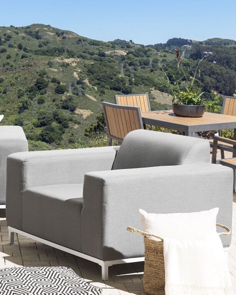 Helle Terrasse mit grauem Sessel, Tisch und Stühlen vor einer grünen Hügellandschaft