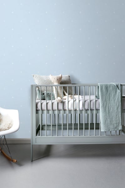 Kinderzimmer mit Gitterbett, Kissen, Kuscheltieren und maritim gemusterter Tapete