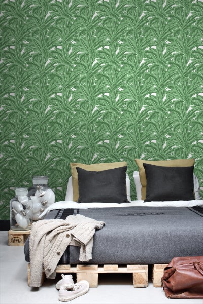 Schlafzimmer mit Wandtapete mit Blattmuster, Bett auf Holzpaletten und dekorativer Glühbirnenvase