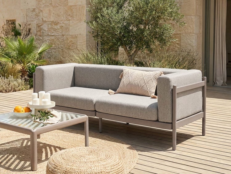 Modernes 2-Sitzer Outdoor-Sofa mit grauen Polstern und Metallgestell auf einer Holzterrasse mit passendem Couchtisch und Jute-Teppich.
