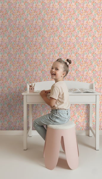 Mädchen sitzt an einem Schreibtisch vor einer Wand mit Blumentapete