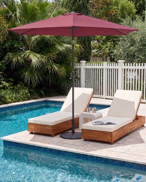 Moderner Außenbereich am Pool mit zwei Sonnenliegen aus Holz mit hellen Auflagen und einem großen Sonnenschirm in einer grünen Gartenumgebung.