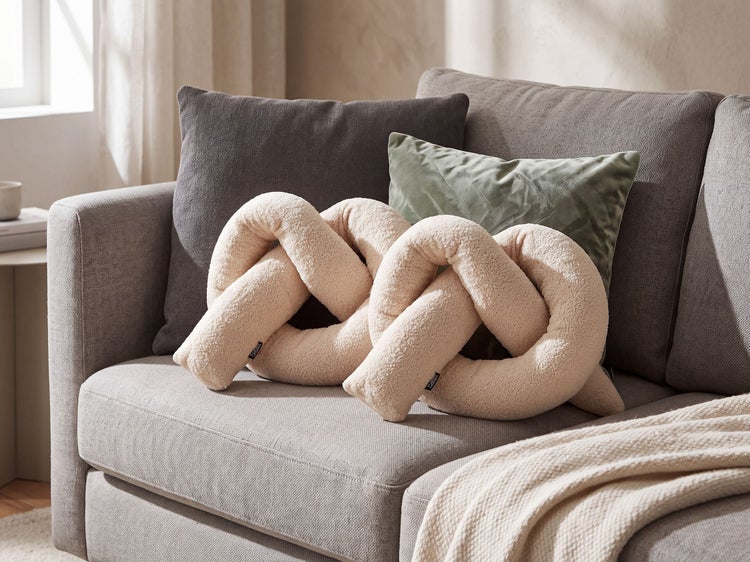 Strukturiertes Knoten-Kissen aus Plüsch in dekorativer Form auf einem gepolsterten Sofa mit weiteren Zierkissen drapiert