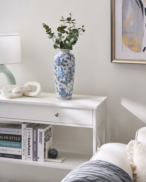 Dekoratives Interieur mit Tisch, Vase mit Pflanzen, Lampe, Deko-Objekt, Büchern und gerahmtem Bild