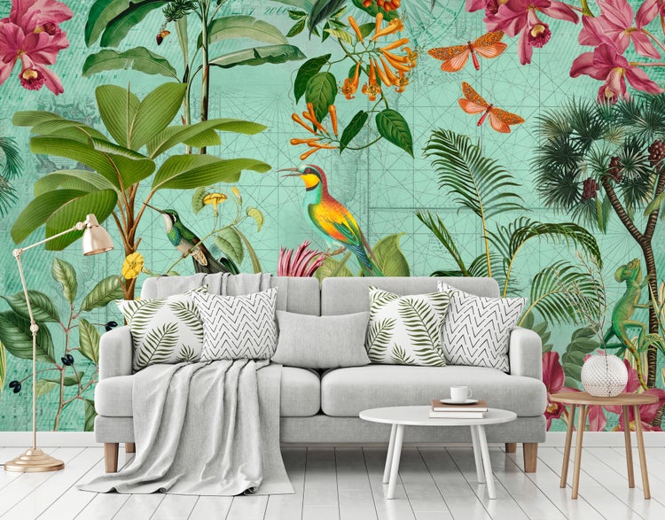 Fototapete mit tropischem Motiv aus Palmen, Orchideen und Vögeln hinter einem grauen Sofa in einem hellen Wohnzimmer.
