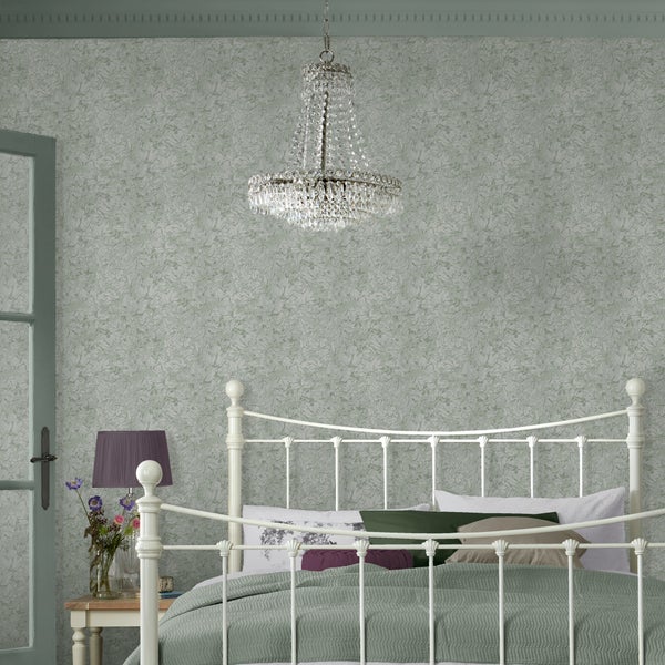 Schlafzimmer mit blumig gemusterter Vliestapete, weißem Metallbett, Kristallkronleuchter und Beistelltisch mit Nachttischlampe im klassischen Stil.
