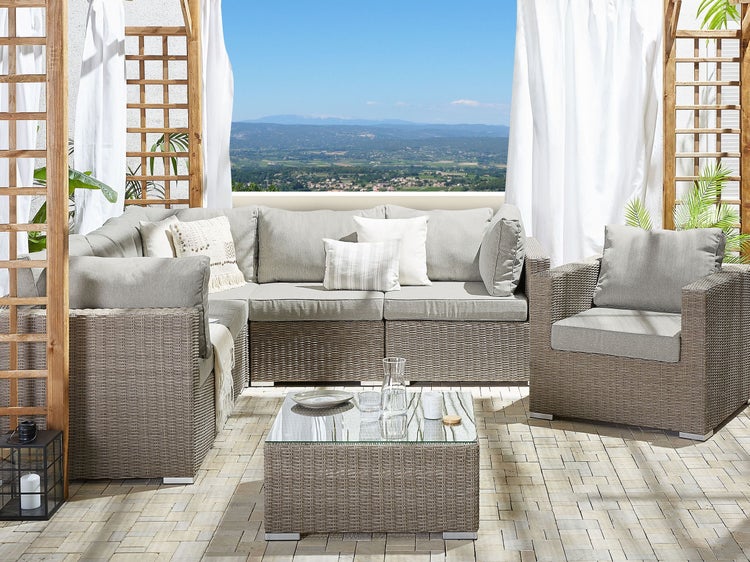 Gartenlounge-Set mit Rattanoptik, bestehend aus Sofa, Sessel und Tisch mit Glasplatte auf einer Terrasse mit Blick auf die Landschaft