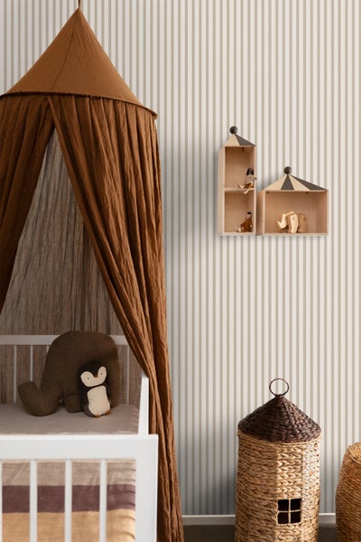 Ein Kinderzimmer mit vertikal gestreifter Tapete, einem weißen Gitterbett unter einem braunen Stoffhimmel sowie Wandregalen aus Holz.