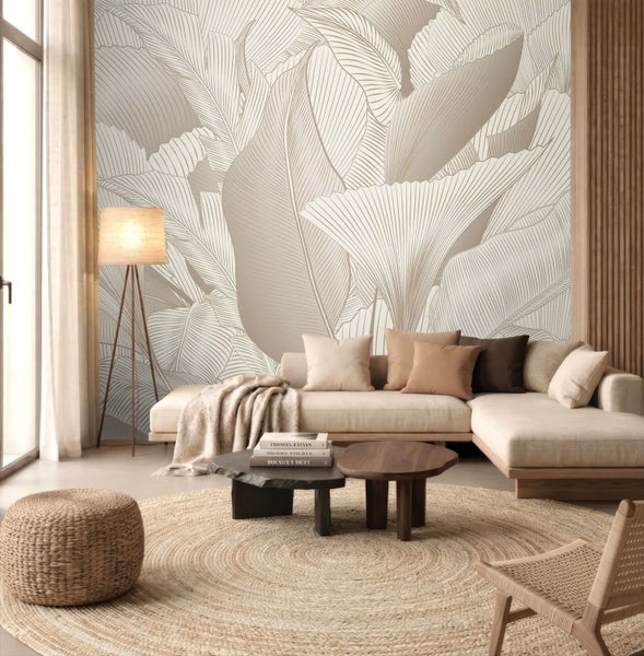 Modernes, helles Wohnzimmer mit einer großformatigen Blätter-Tapete, einem hellen Ecksofa, runden Holztischen und einem runden Naturfaserteppich.