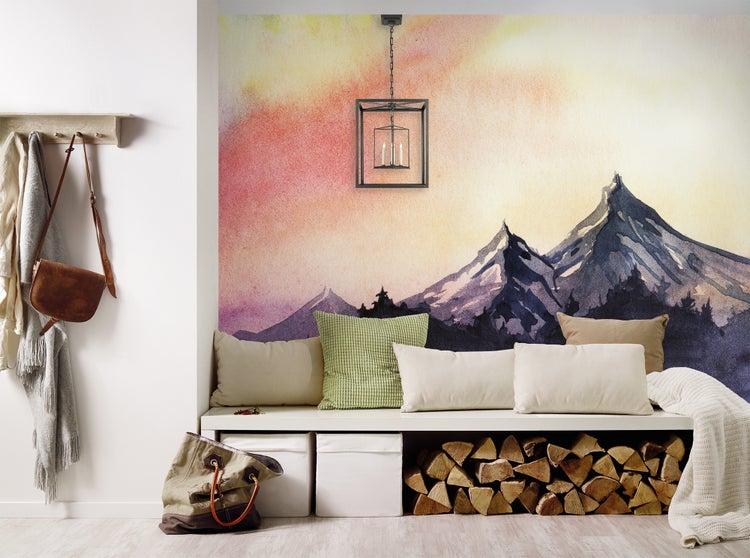 Fototapete mit Aquarell-Berglandschaft in einem hellen, organisierten Raum mit weißer Sitzbank, Kissen, Kaminholz-Aufbewahrung und Pendelleuchte.