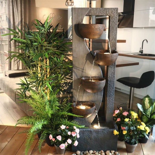 Dekorativer Zimmerbrunnen mit mehreren Schalen und Pflanzen in Wohnraum.