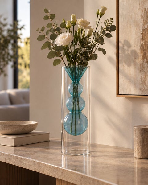 Moderne Glasvase mit innenliegendem blauen Glaskörper und Blumenstrauß auf einem Tisch in einem hellen Wohnraum.