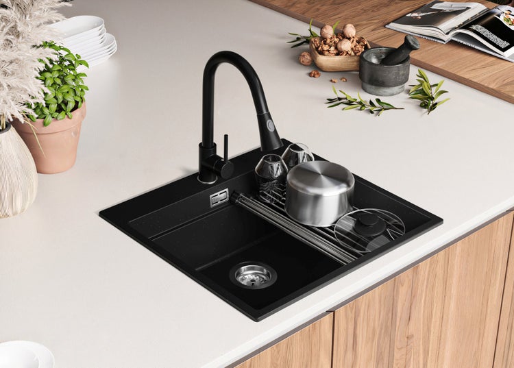 Schwarzes Küchenspülbecken mit Armatur, Abtropfgestell und Küchenutensilien auf einer Küchentheke.