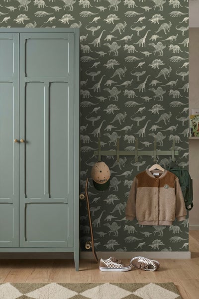 Kinderzimmer mit Dinosaurier-Tapete, Schrank, Wandgarderobe mit Jacke und Rucksack, Skateboard und Schuhen auf Holzboden.