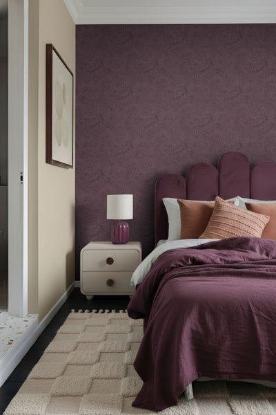 Schlafzimmer mit Bett, Nachttisch, Lampe und gemusterter Tapete