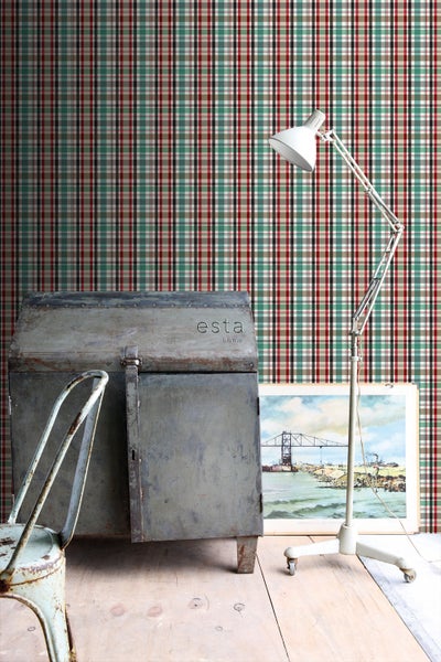 Raumansicht mit karierter Tapete, einer Stehlampe, einer Metalltruhe mit dem Esta Home Logo, einem Stuhl und einem Bild mit einer Brücke.