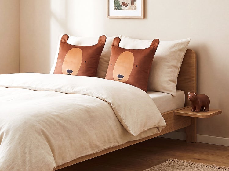 Zwei quadratische Dekokissen in Bärenform auf einem Bett mit beigefarbener Bettwäsche in einem modern eingerichteten Schlafzimmer.