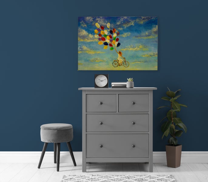 Wandbild mit Motiv einer Frau auf einem Fahrrad mit Luftballons, hängend über einer grauen Kommode in einem modern eingerichteten Raum.