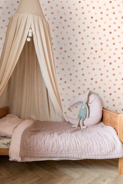 Kinderzimmer mit Himmelbett, Wandtapete mit Punktmuster und einem Stofftier auf dem Bett.