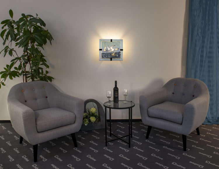 Einladende Sitzecke mit zwei grauen Sesseln, einem Beistelltisch mit Wein und Gläsern, einer Wandleuchte und einer Zimmerpflanze.