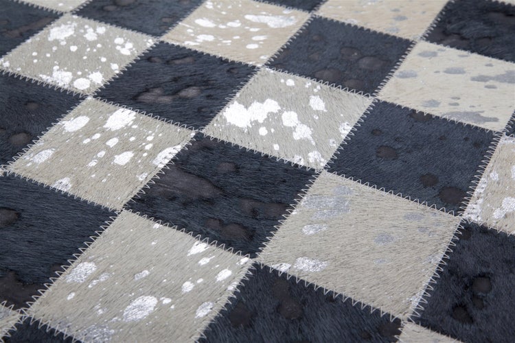 Patchwork-Teppich aus Kuhfell mit schwarz-weißen Karos, silbernen Metallic-Effekten und sichtbaren Zickzack-Nähten.