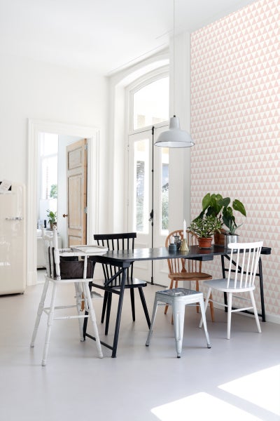 Heller Raum mit Esstisch, verschiedenen Stühlen und Tapete mit Dreiecksmuster