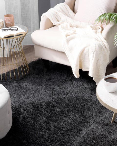 Schwarzer Langflor Teppich in einem Wohnzimmer mit Sessel und Beistelltischen.