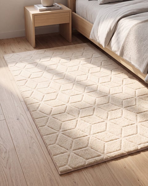 Wohnteppich mit geometrischem Rautenmuster in einem modern eingerichteten Schlafzimmer auf einem Holzboden.