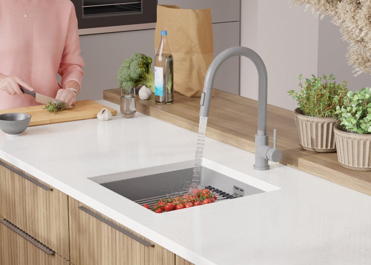 Küchenszene mit Spüle, Armatur und Person beim Zubereiten von Speisen.