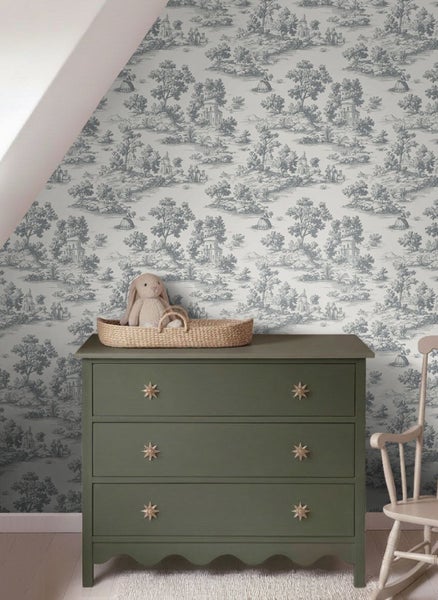 Tapete mit ländlichem Toile-de-Jouy-Muster in einem hellen Zimmer hinter einer Kommode mit dekorativen Griffen und einem Korb mit Stofftier.