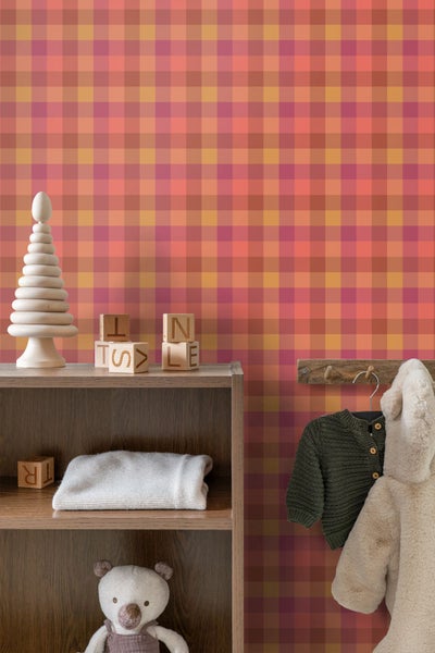 Karo-Tapete in warmen Rot- und Orangetönen in einem organisierten Kinderzimmer mit Holzregal, Holzspielzeug und Kinderkleidung.