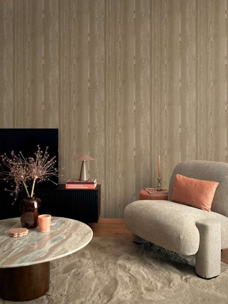 Wohnzimmer mit Vliestapete in Holzoptik mit vertikaler Maserung, kombiniert mit einem modernen Sessel und einem runden Couchtisch aus Stein.