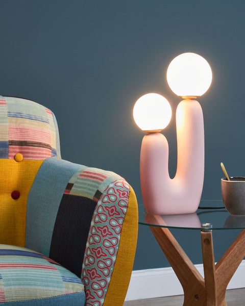 Dekorative Tischleuchte mit zwei Leuchtkörpern auf einem Beistelltisch neben einem Sessel