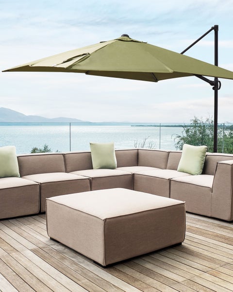 Moderner Ampelschirm über einem hellbraunen Lounge-Set auf einer Holzterrasse mit Wasserblick.