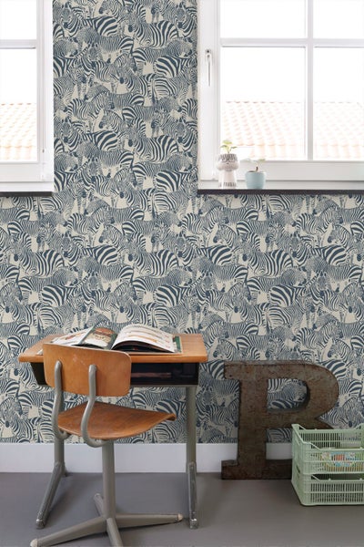 Vliestapete mit flächendeckendem Zebra-Muster in einem hellen Zimmer mit Schreibtisch, Holzstuhl und Fenster.