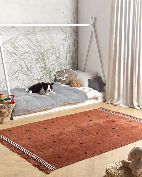 Helles Kinderzimmer mit Hausbett aus Holz, Fototapete mit Gräsern und einem rostbraunen Teppich mit Punkten auf hellem Holzboden.
