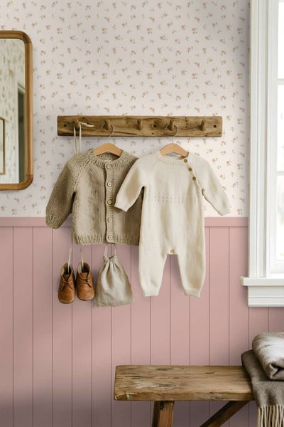 Wohnraum mit gemusterter Tapete mit Blumenmotiv und halbhoher Wandvertäfelung, hölzerner Garderobenleiste mit Kinderkleidung und einer Sitzbank.