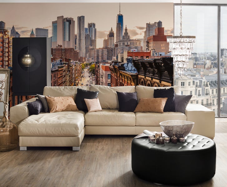 Fototapete mit New York Skyline in einem modernen Wohnzimmer mit hellem Ecksofa, schwarzem Hocker und Parkettboden.