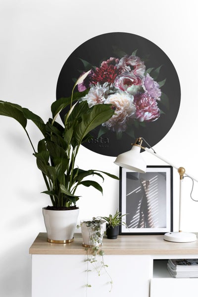 Dekoratives Interieur mit Zimmerpflanzen, Lampe und einem runden Wandbild mit Blumenmuster.