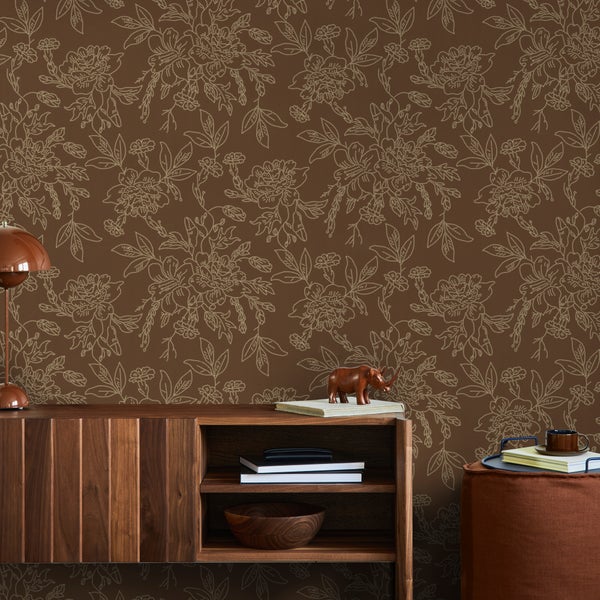 Vliestapete mit filigranem floralem Muster in einem geordneten Wohnzimmer hinter einem Sideboard aus Holz.