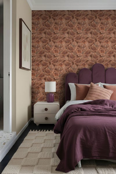 Schlafzimmer mit gemusterter Tapete, Nachttisch und Bett mit lila Tagesdecke