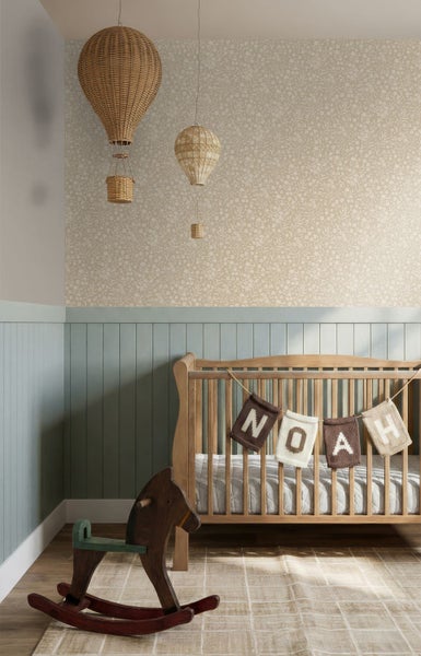 Kinderzimmer mit floraler Tapete und hellblauer Holzvertäfelung. Babybett aus Holz, Schaukelpferd und geflochtene Heißluftballons als Dekoration.