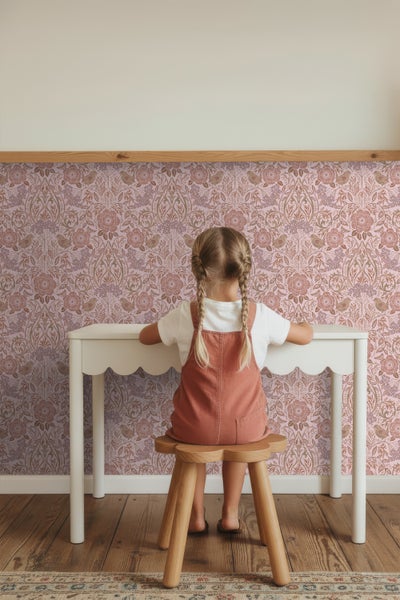 Mädchen sitzt an einem weißen Schreibtisch vor einer floral gemusterten Tapete.