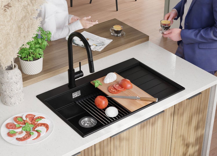 Schwarzes Spülbecken mit Abtropffläche, Wasserhahn, Schneidebrett, Tomaten und Mozzarella in einer Küchentheke