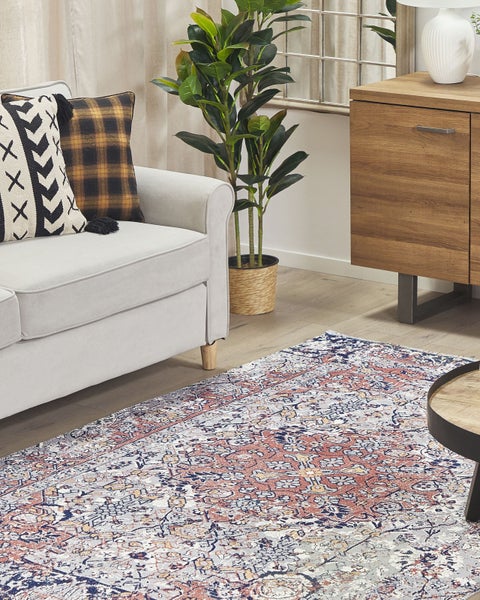 Orientteppich mit filigranem Muster in einem hellen Wohnzimmer neben einem grauen Sofa, einer Zimmerpflanze und einem Sideboard aus Holz.