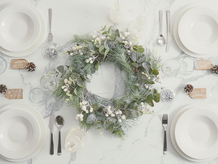 Festlich gedeckter Esstisch mit weißem Geschirr, Silberbesteck und einem winterlichen Kranz als Dekoration.