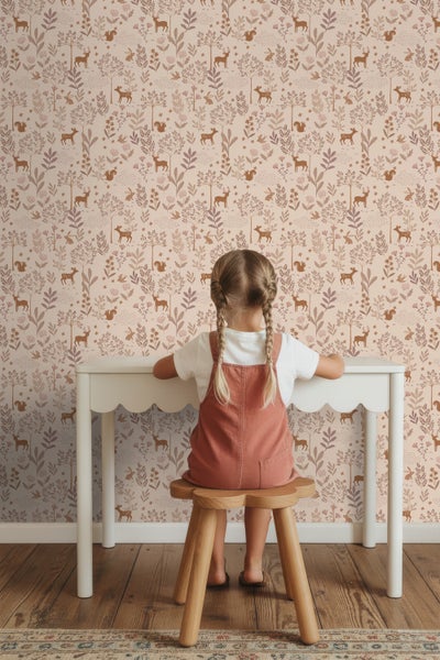 Kind sitzt an Tisch vor einer Tapete mit Waldtier- und Pflanzenmuster.