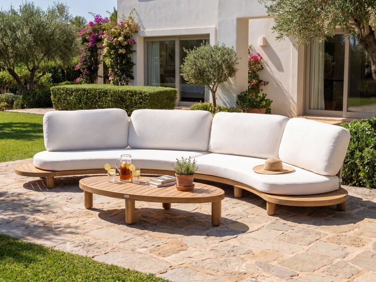 Geschwungenes Garten-Lounge-Set aus Holz mit weißen Polstern auf einer Steinterrasse vor einem hellen Haus im Garten.