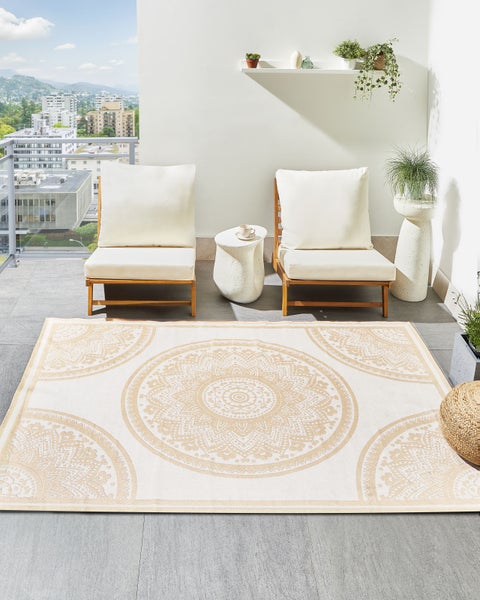Heller Outdoor-Teppich mit runden Mandala-Mustern in Beige auf einem modernen Balkon mit Holzsesseln und hellen Polstern.