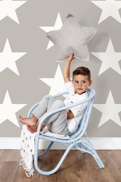 Junge sitzt in einem blauen Sessel und hält ein Sternenkissen vor einer Wand mit Sternenmuster